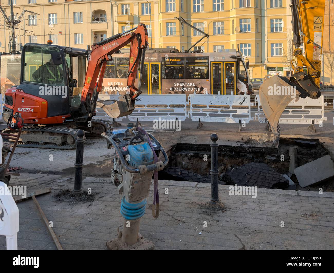 Pozna, Polonia – 3 marzo 2026: Un escavatore industriale JCB giallo si trova vicino a una buca nel marciapiede in mezzo ai lavori di ricostruzione di una strada cittadina affollata dove lui Foto Stock