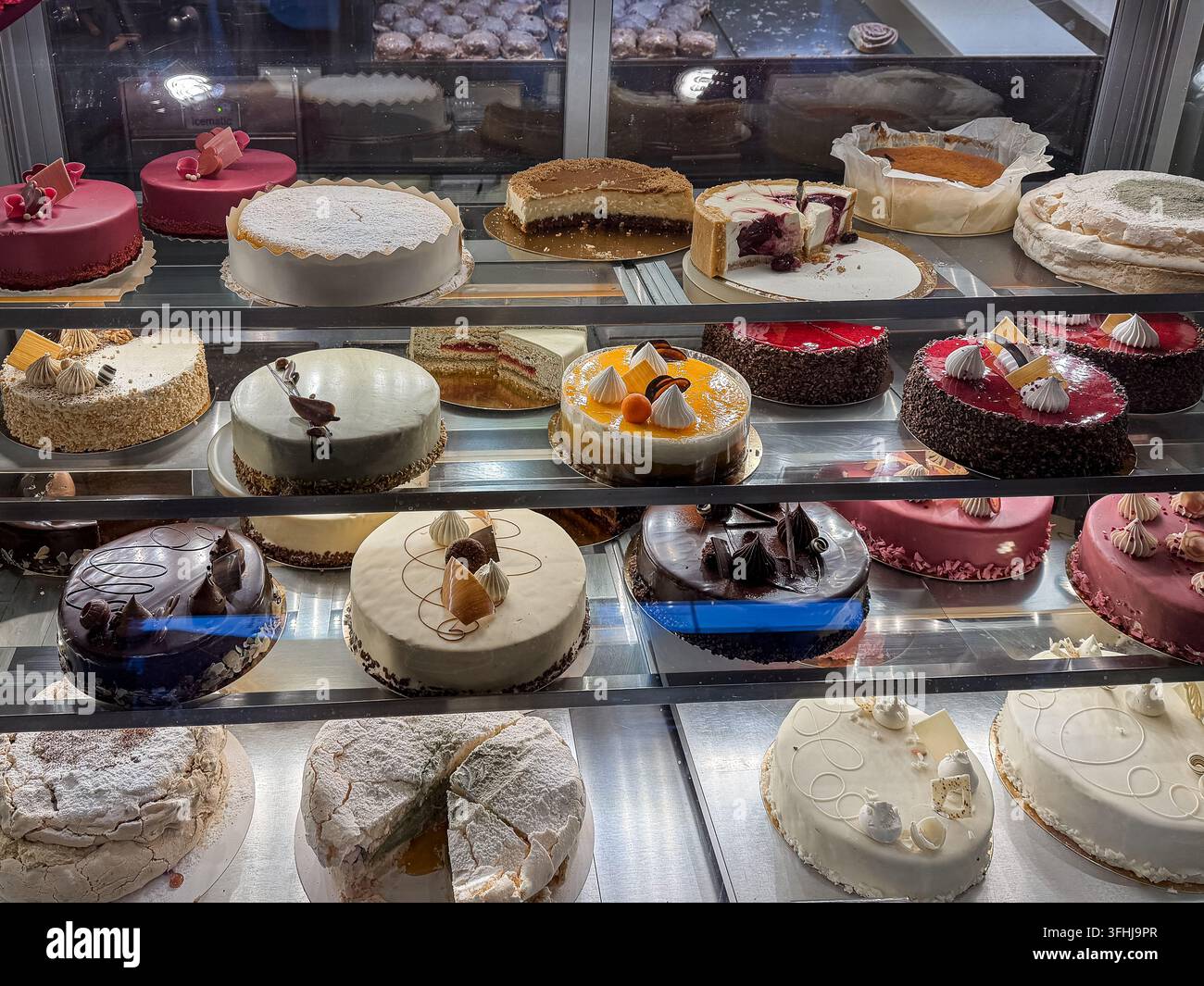 Vari torte artigianali appena sfornate disposte all'interno di una vetrina refrigerata al dettaglio, che offre una varietà allettante di dolci per feste, catering Foto Stock