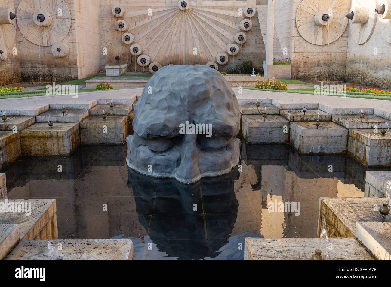 Una sorprendente scultura in pietra di una testa in una fontana, su uno sfondo architettonico ornato. Foto Stock