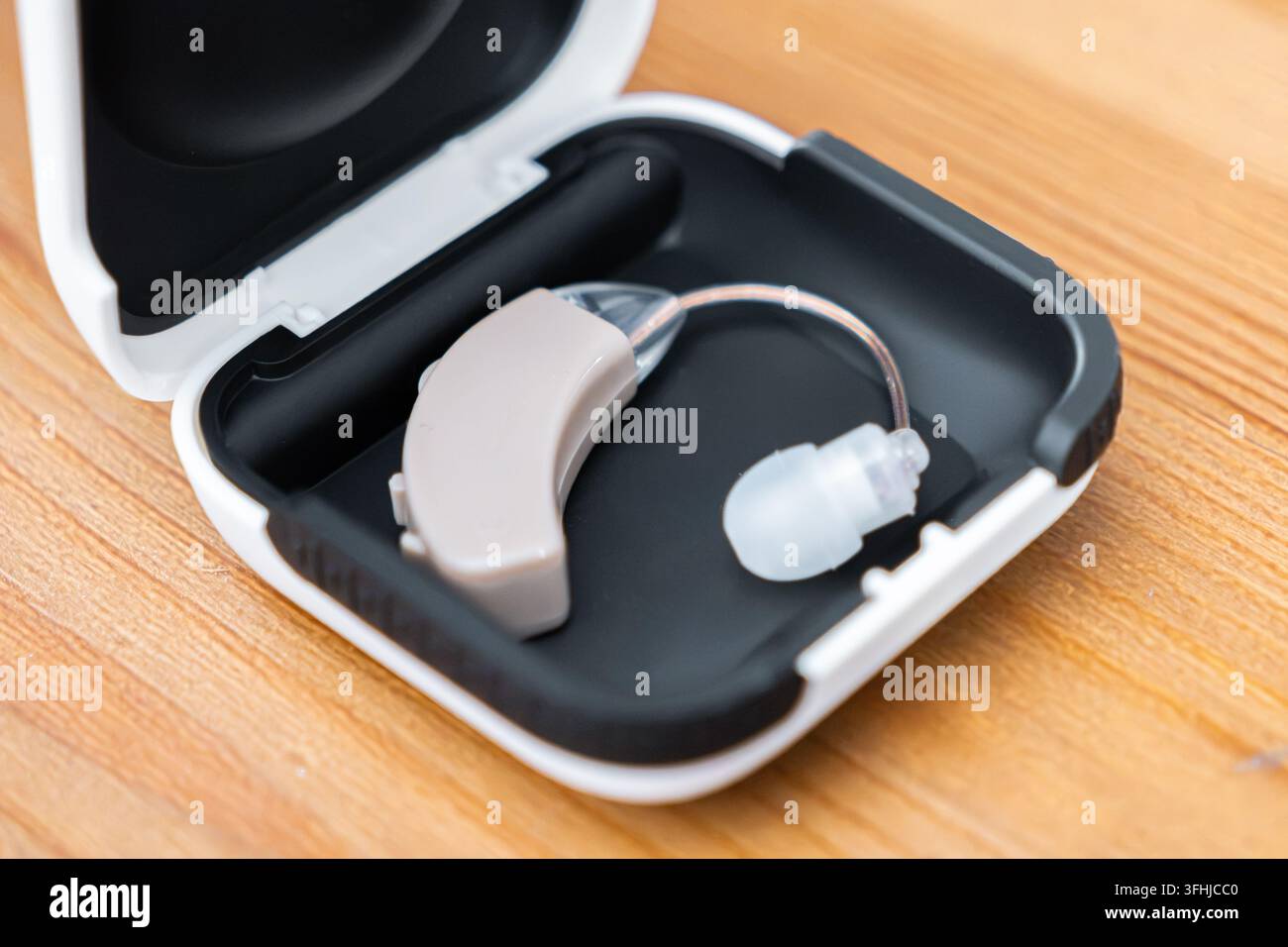 Dispositivo uditivo moderno si trova all'interno di un contenitore di plastica nero aperto posizionato su una scrivania, rappresentando una tecnologia medica professionale per la riabilitazione uditiva Foto Stock
