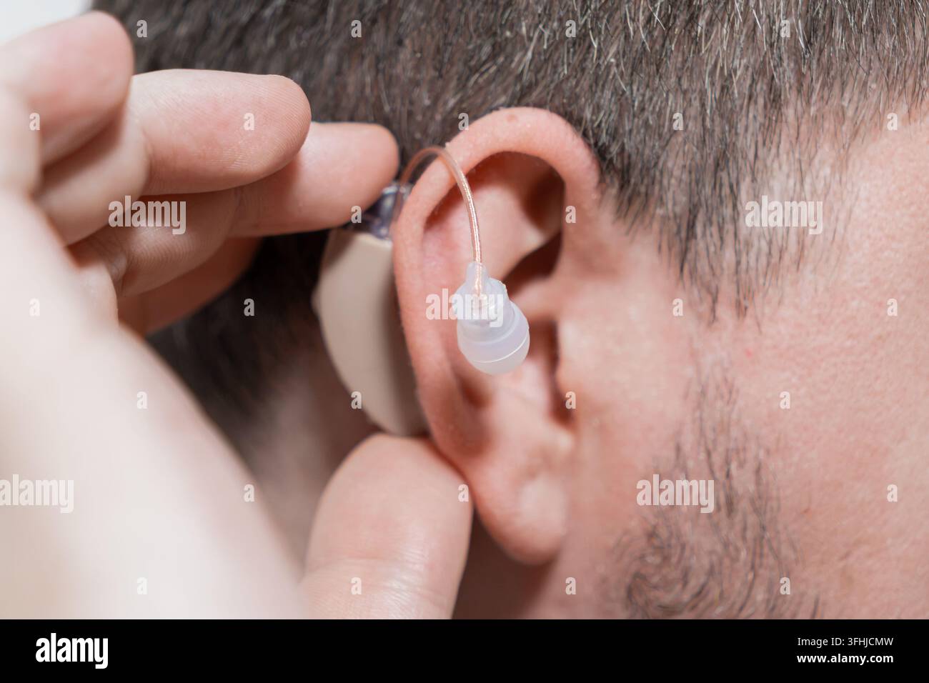 Persona che inserisce un dispositivo uditivo compatto nel condotto uditivo, dimostrando un'assistenza efficace per individui con perdita uditiva in un ambiente clinico Foto Stock