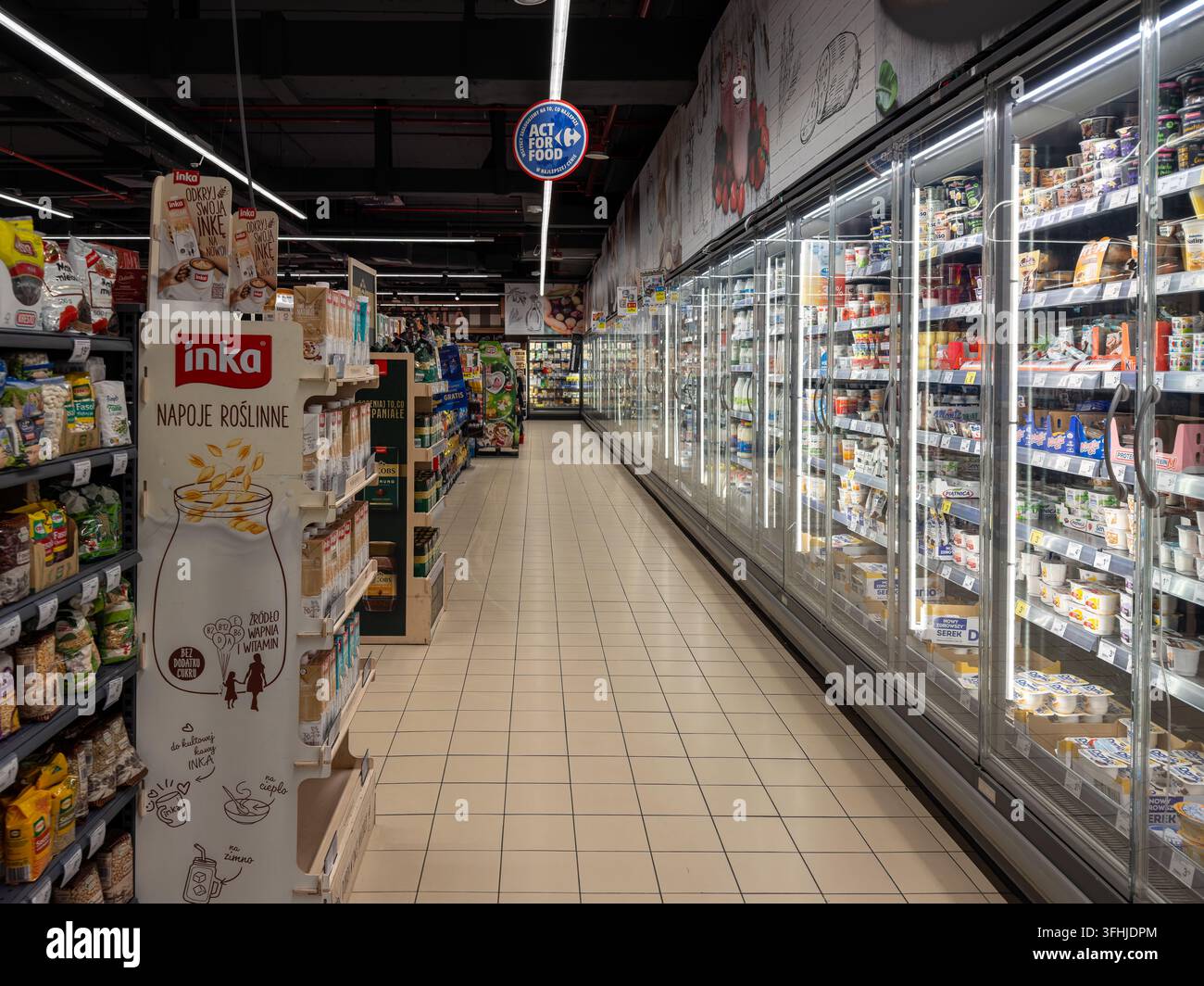 Pozna, Polonia - 16 gennaio 2026: Un corridoio del negozio Carrefour mostra armadi refrigerati illuminati pieni di vari alimenti accanto a un'esposizione s Foto Stock