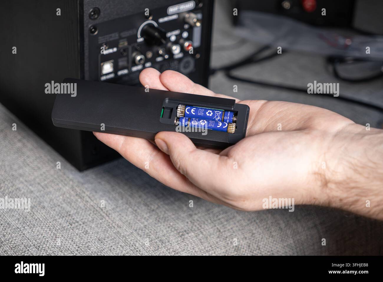 Una persona inserisce piccole celle energetiche blu all'interno di un alloggiamento per telecomando per attivare un sistema audio senza fili, catturando il processo di risoluzione dei problemi dell'impianto home entertainment Foto Stock