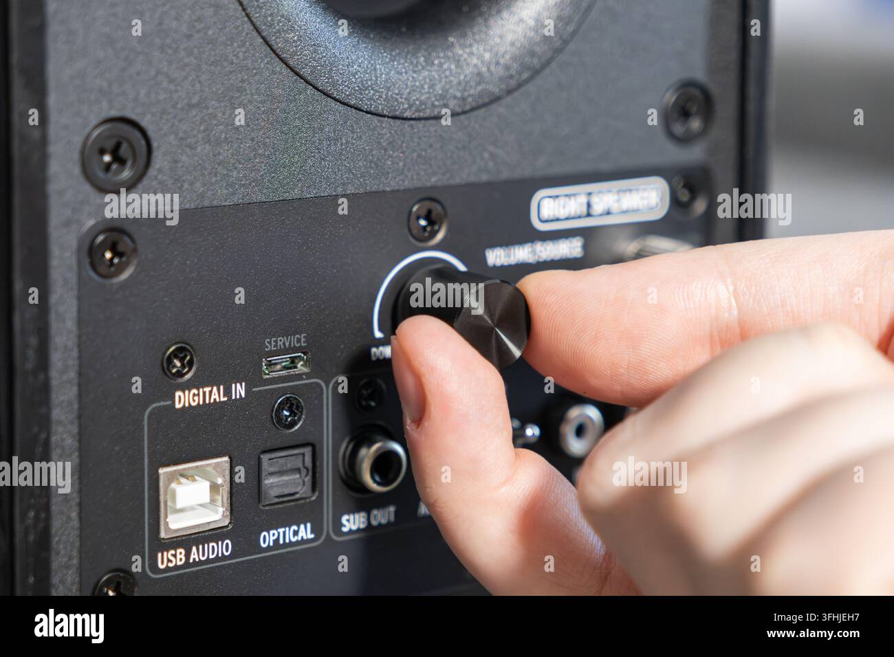 Le dita girano una manopola di controllo in metallo nero su un monitor multimediale per regolare con precisione le impostazioni del volume, mostrando una manipolazione manuale precisa dell'hardware in Foto Stock