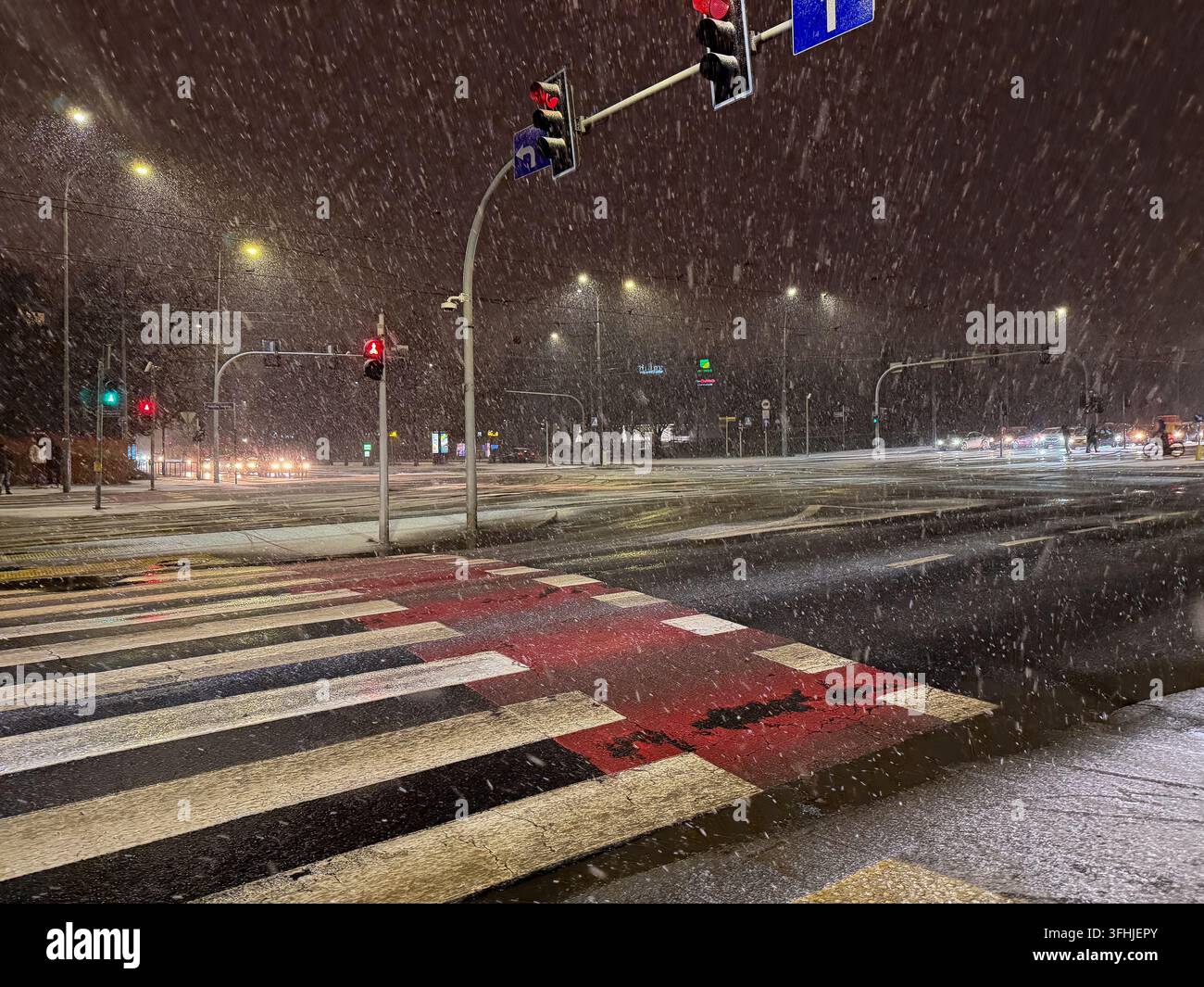 Forti nevicate cadono su un incrocio cittadino buio sotto lampioni luminosi, enfatizzando un'atmosfera metropolitana tranquilla ma attiva durante le condizioni invernali su Foto Stock