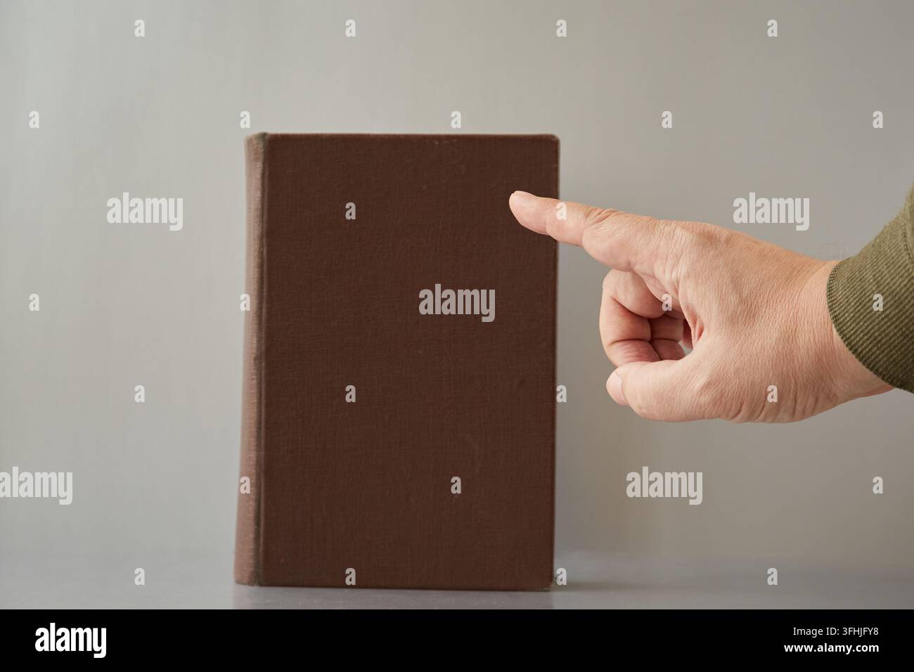 Una mano con un dito puntato che indica un vecchio libro senza titolo sulla copertina. Foto Stock