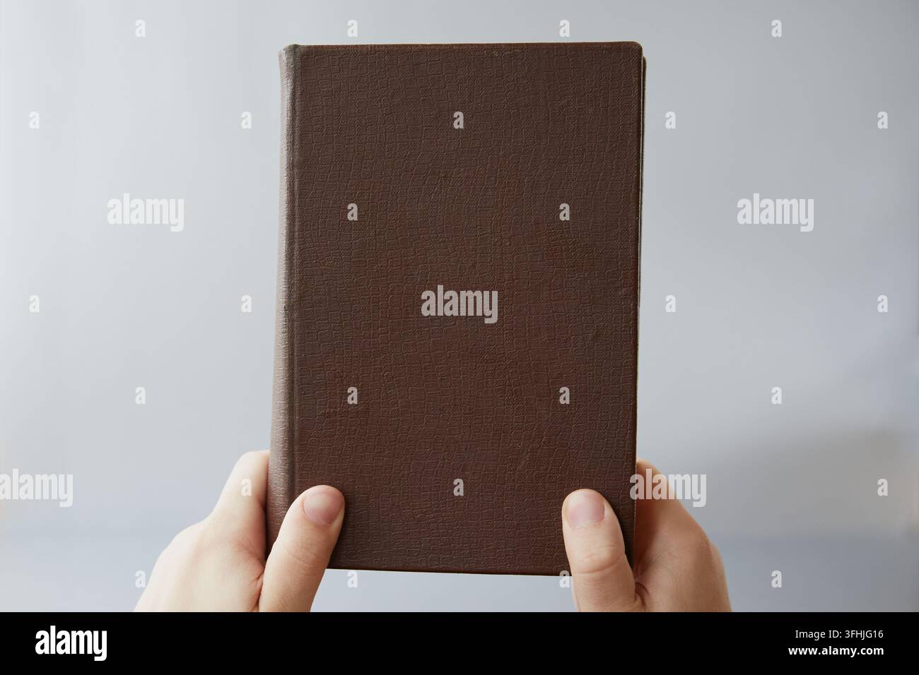 Un vecchio libro con copertina marrone senza titolo tenuto da due mani, primo piano. Antica legge, verità bibliche Foto Stock