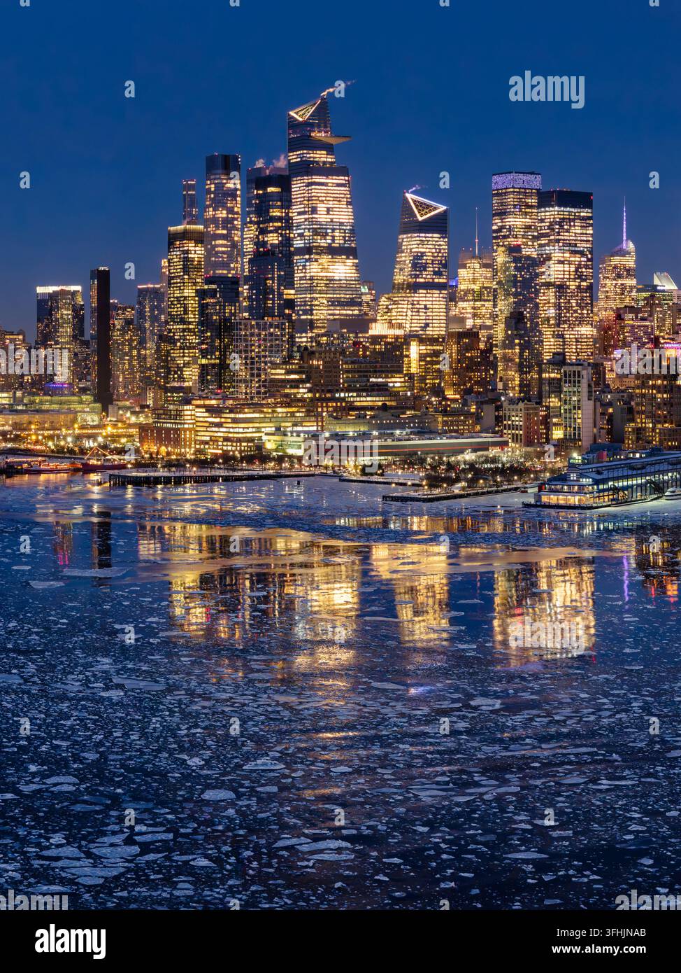 Vista aerea invernale dello skyline di Manhattan con i grattacieli di Hudson Yards illuminati al crepuscolo. Fiume Hudson ghiacciato con ghiaccio galleggiante. New York City Foto Stock
