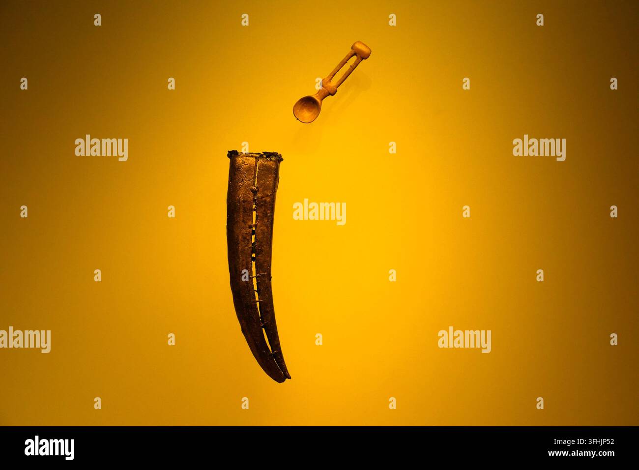 BOGOTA, COLOMBIA - 11 NOVEMBRE 2025: Artefatti d'oro precolombiani tra cui un corno cerimoniale e un cucchiaio ornato esposti su uno sfondo giallo vivace Foto Stock