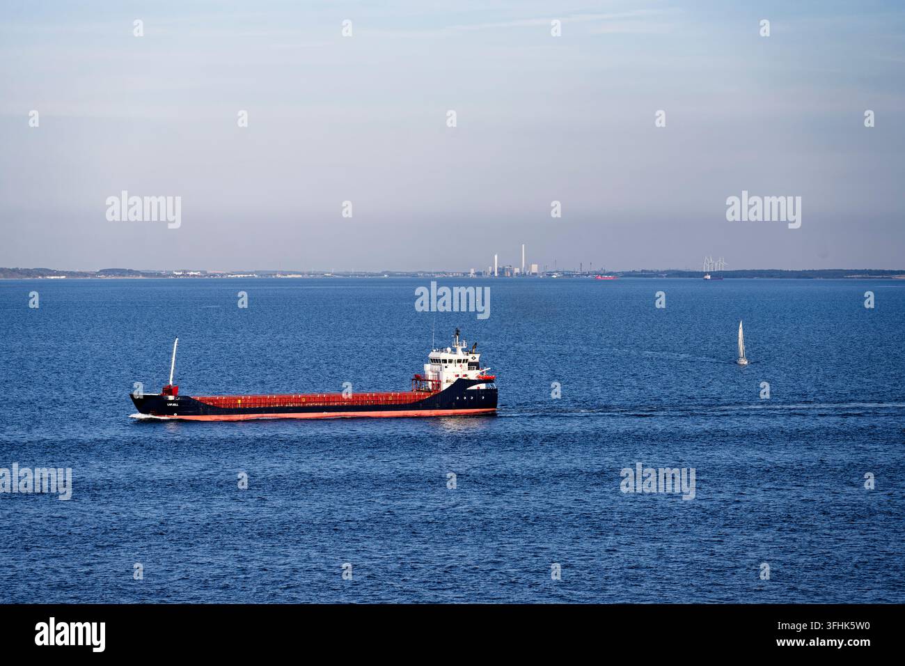 Great Belt Danimarca, nave merci generale Lafjell in movimento attraverso il mare blu con costa industriale sullo sfondo Foto Stock