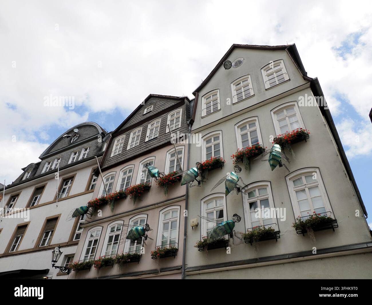 Sculture di angeli in metallo stravaganti decorano le facciate degli edifici storici tradizionali tedeschi con fioriere rosse a Marburg. Foto Stock