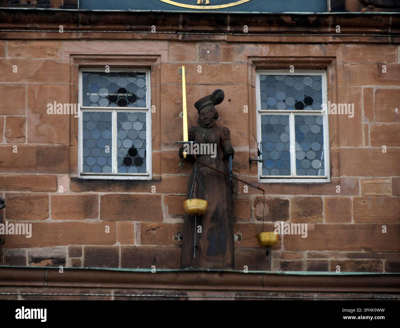 Statua in pietra della Giustizia con bilance dorate e spada montata sulla facciata in arenaria del Municipio di Marburg, Germania. Foto Stock
