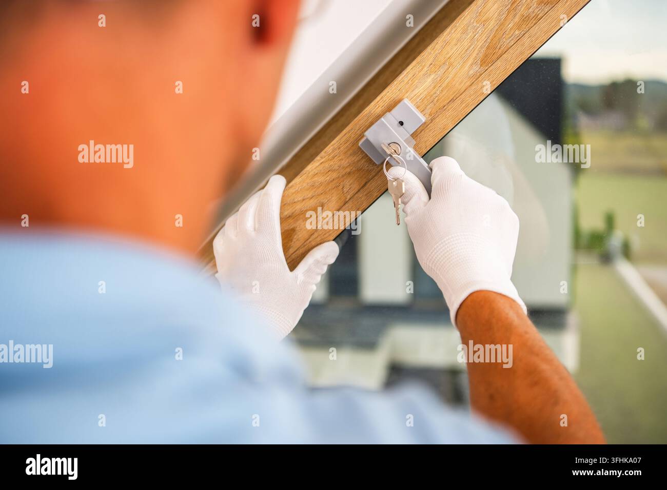 Un operaio che indossa guanti tiene una chiave nella serratura della maniglia di una finestra mentre con l'altra mano sostiene il telaio della finestra. Foto Stock