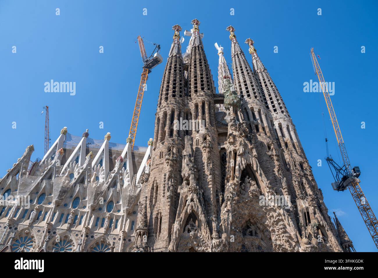 Iconica basilica della Sagrada Família a Barcellona, Spagna, che mostra l'intreccio lavoro in pietra di Gaudí, torri svettanti e gru in mezzo alla costruzione in corso; drammatico Foto Stock