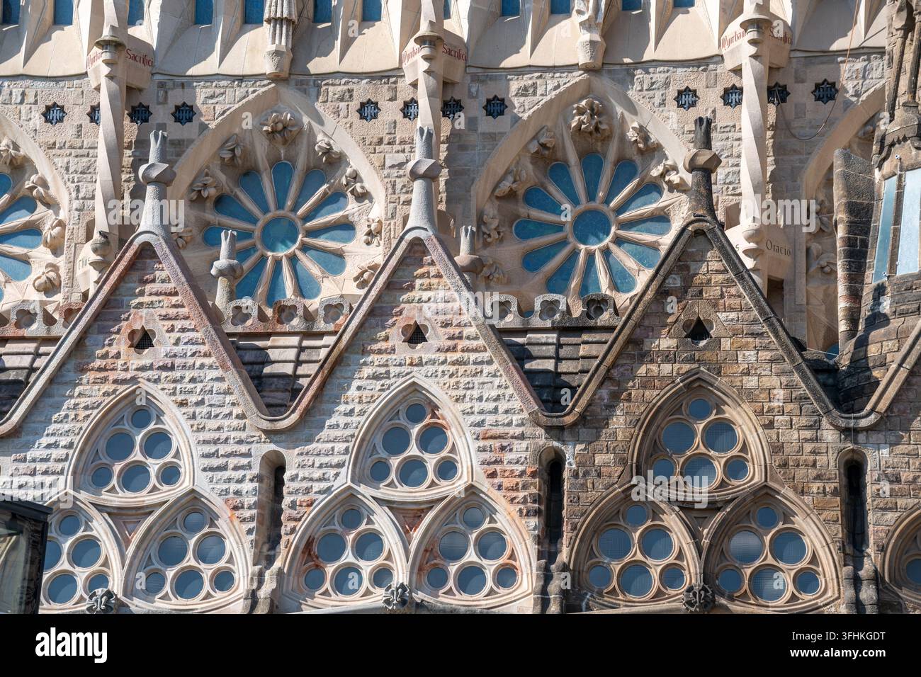 Dettagli ornati della facciata e finestre rotonde a rosone della basilica Sagrada Familia mostrano lo stile neogotico modernista di Antoni Gaudí, pietra strutturata Foto Stock