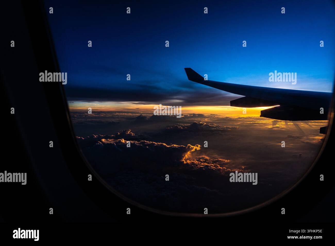 Una vista serena del tramonto da un finestrino dell'aereo, che mostra cieli colorati e formazioni nuvolose sopra la superficie terrestre. Foto Stock