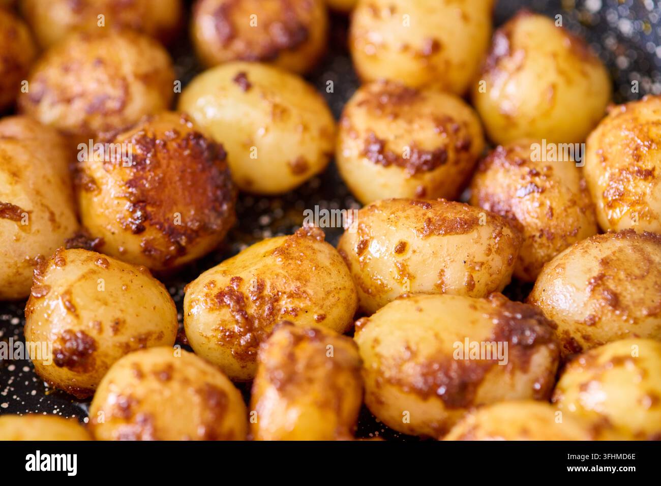 Patatine dorate fritte arrosto perfette croccanti con condimento saporito in padella nera, luce calda evidenzia la texture e il colore appetitosi Foto Stock