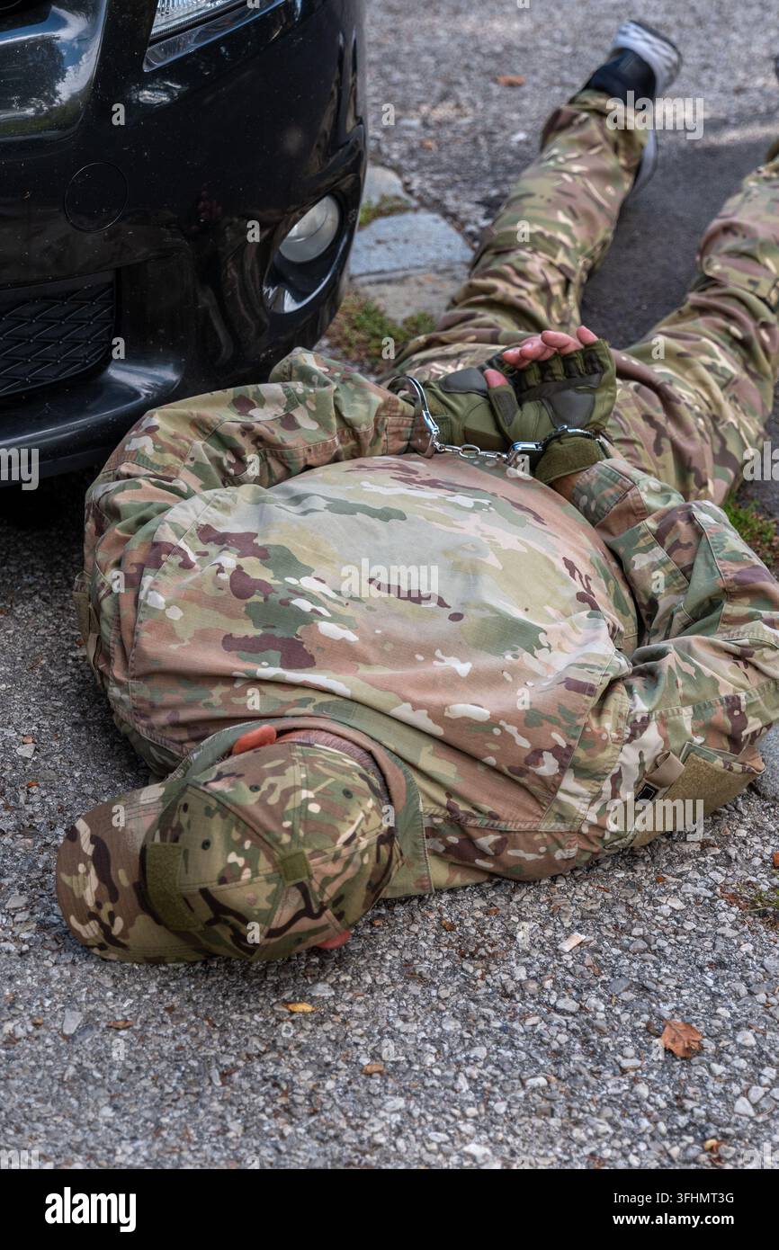 Uomo in mimetica militare legato accanto a un veicolo dopo un arresto simulato da parte del servizio di sicurezza Foto Stock