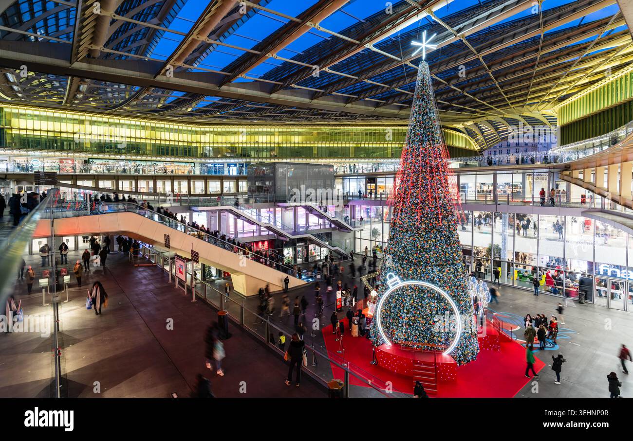 Parigi, Francia - 24 dicembre 2025: Un grande albero di Natale decorato all'interno del centro commerciale Forum des Halles sotto la moderna cupola di vetro. Foto Stock