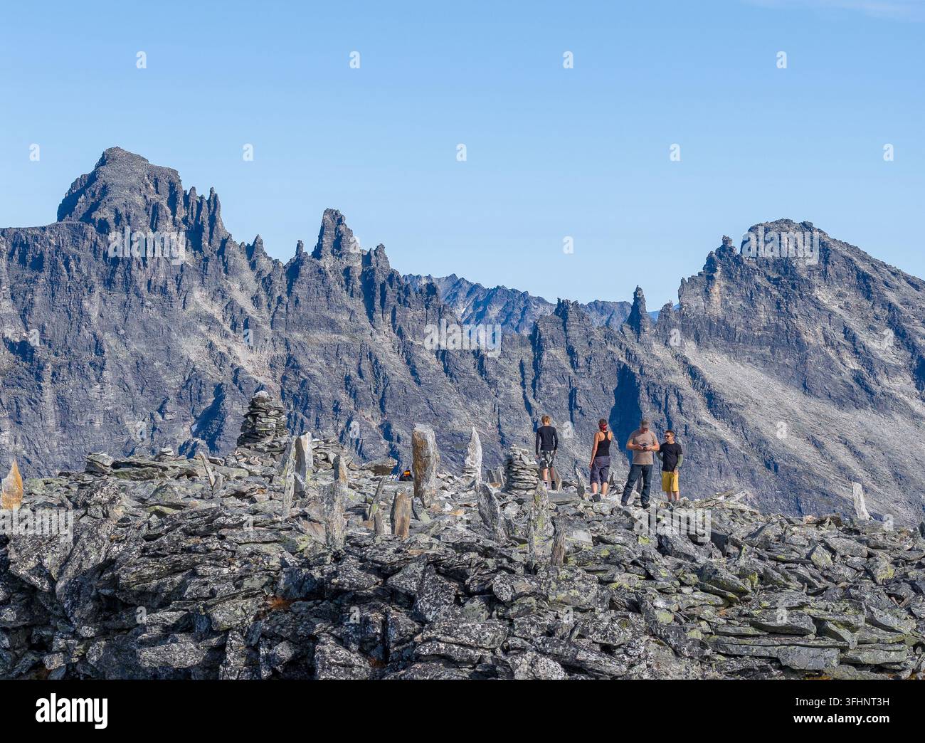 Vista aerea del picco del monte Kongen con escursionisti su una cresta rocciosa circondata da cumuli di pietre sotto un cielo blu terso nel comune di Rauma, Mor Foto Stock