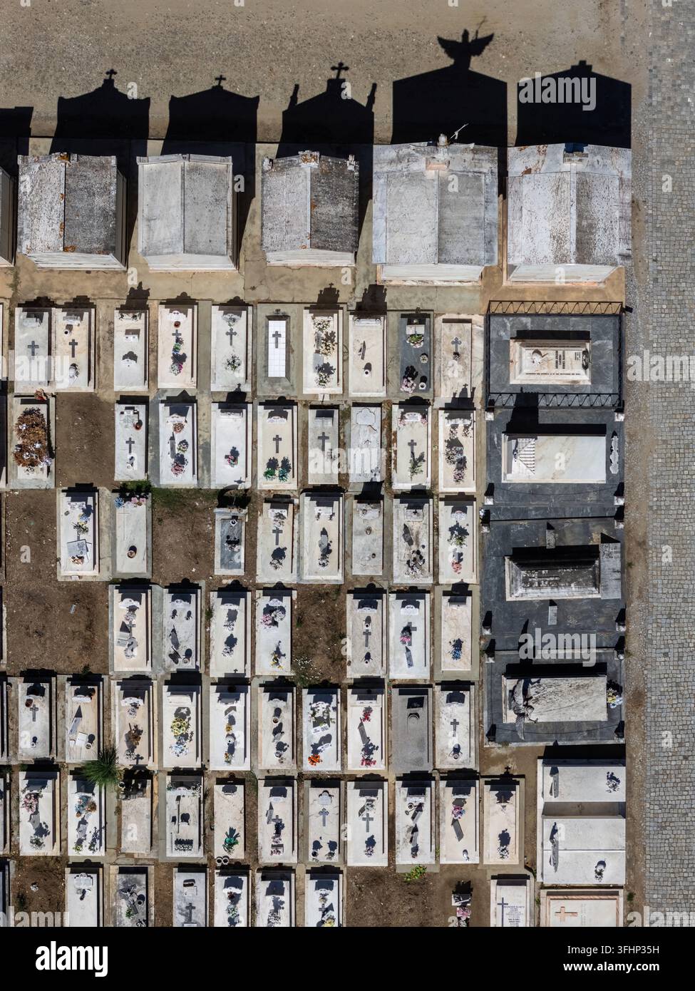 Vista aerea di un cimitero con file di tombe in pietra bianca, croci e lunghe ombre proiettate dai monumenti a Évora, distretto di Évora, Portogallo. Foto Stock