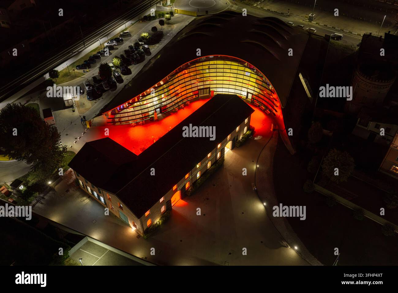 Vista aerea del Museo Enzo Ferrari con il suo iconico tetto giallo e il cortile illuminato di notte a Modena, Emilia-Romagna, Italia. Foto Stock