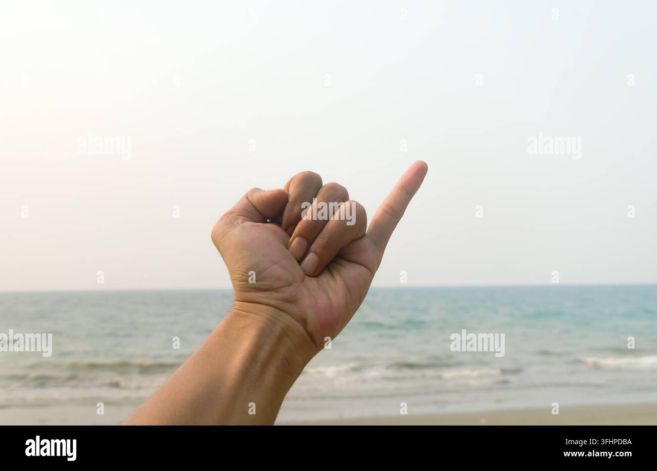 Primo piano di una mano che fa una promessa con il mignolo o un gesto con il mignolo su una spiaggia tropicale Foto Stock