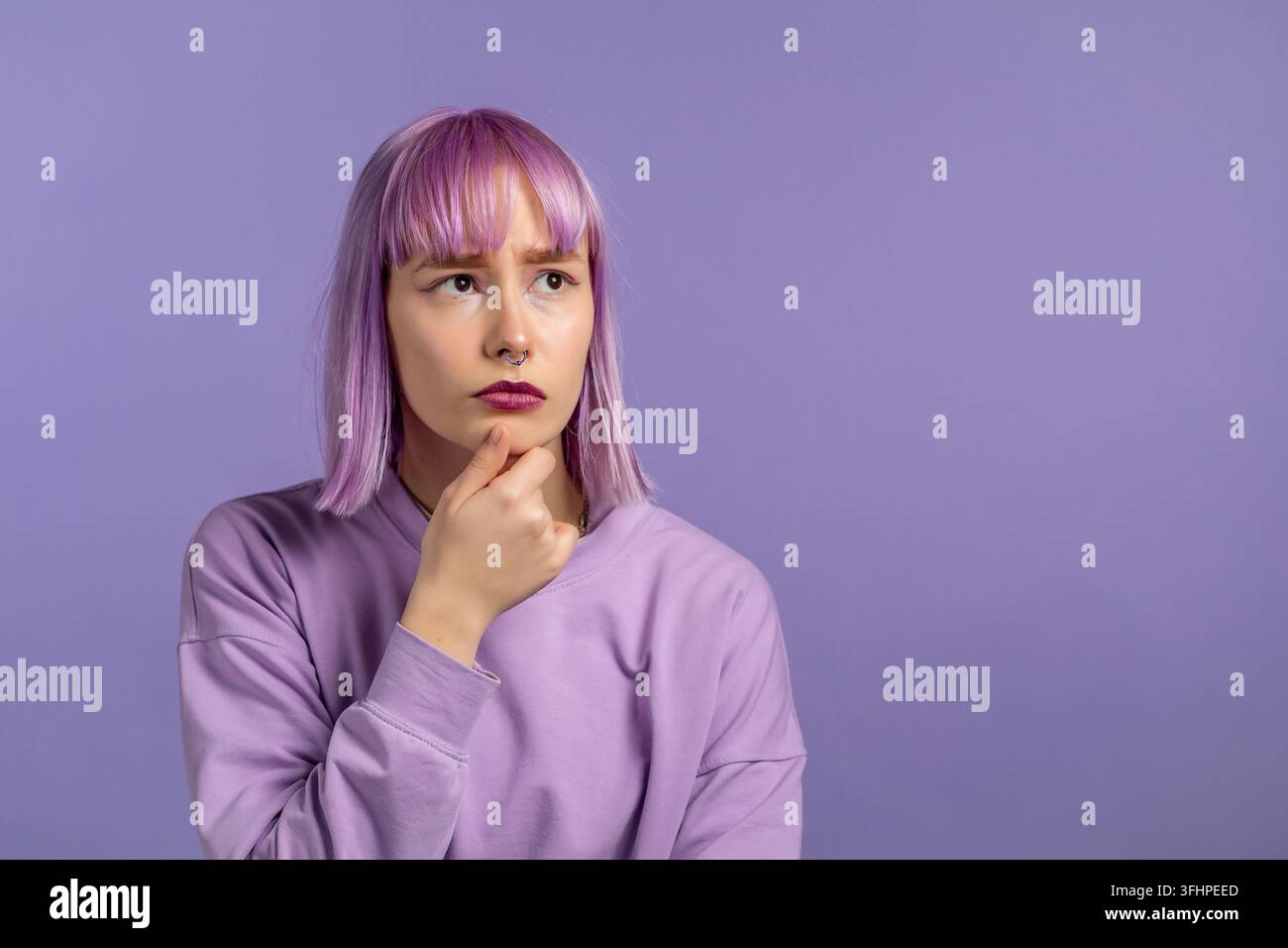 Donna pensierosa con capelli tinti di viola che guarda verso l'alto su uno sfondo viola in studio. Espressioni facciali pensierose. Bella modella con attraente Foto Stock