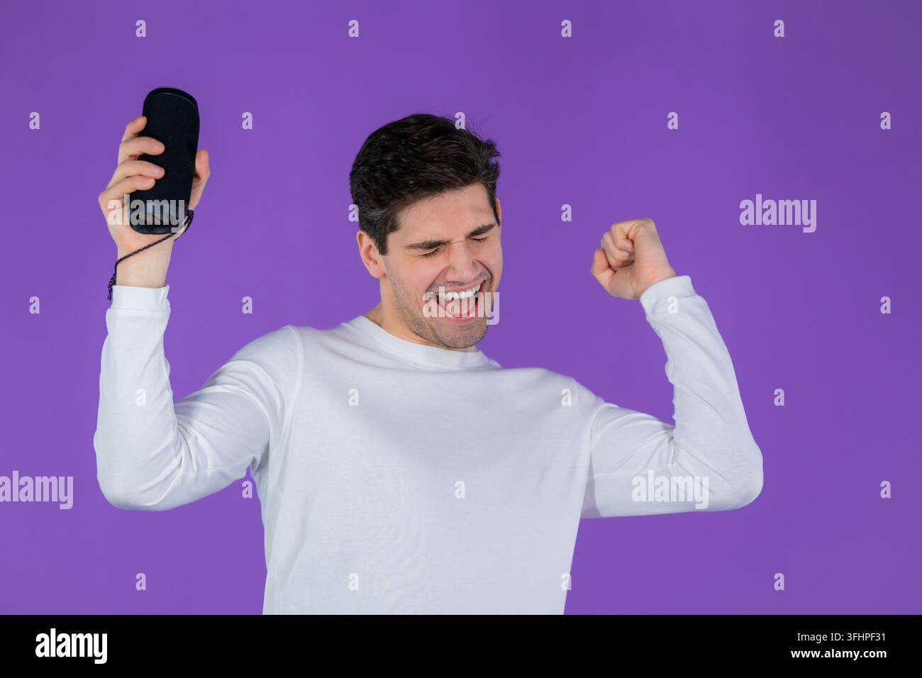 Uomo che ascolta musica con un altoparlante portatile senza fili – sistema audio moderno. Giovane che balla, si diverte su uno sfondo viola dello studio Foto Stock