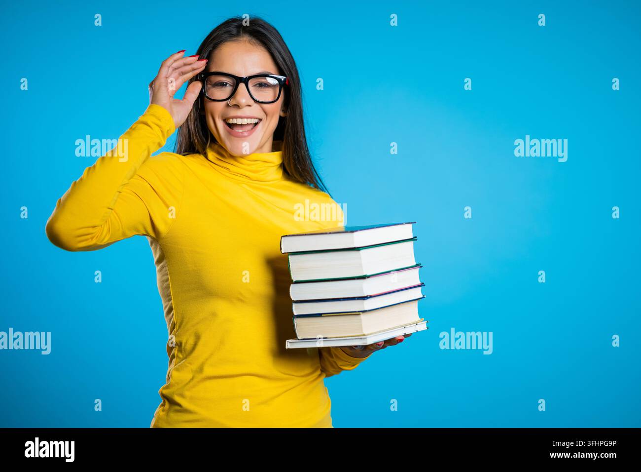 Studentessa di latino su sfondo blu in studio tiene una pila di libri universitari della biblioteca. Foto Stock