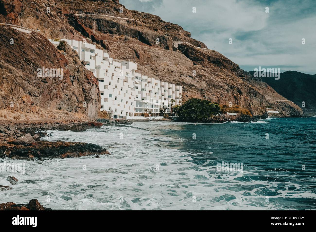 Vista sull'oceano Pacifico con edificio bianco a più piani, paesaggio marino, superficie dell'acqua, increspature, piccole onde su una spiaggia di ciottoli. Universale na Foto Stock