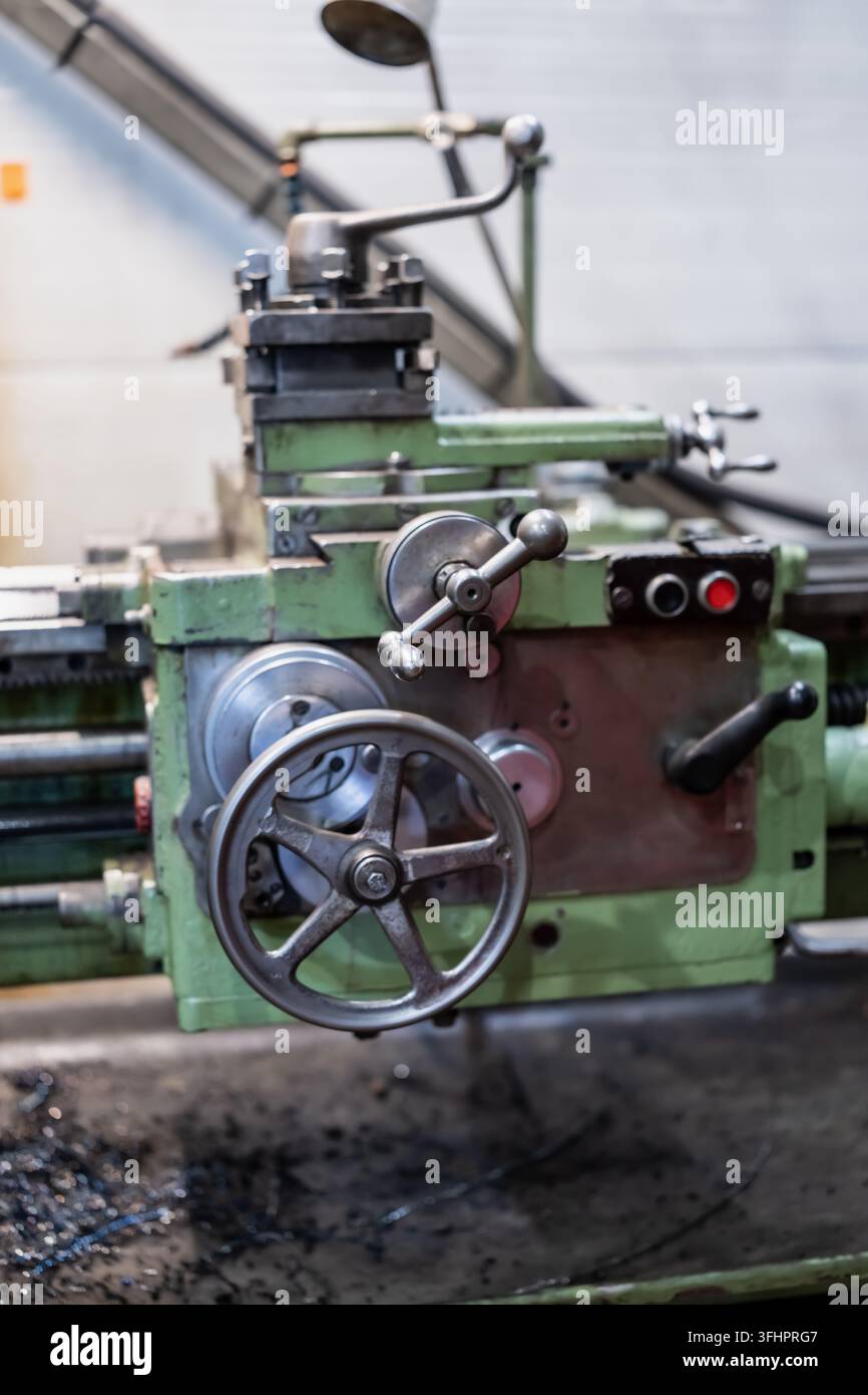 Tornio manuale per la lavorazione dei metalli con volantini del carro, leve di controllo e un portautensili sopra i trucioli metallici, che illustra l'attrezzatura per la tornitura e il lavoro qualificato Foto Stock