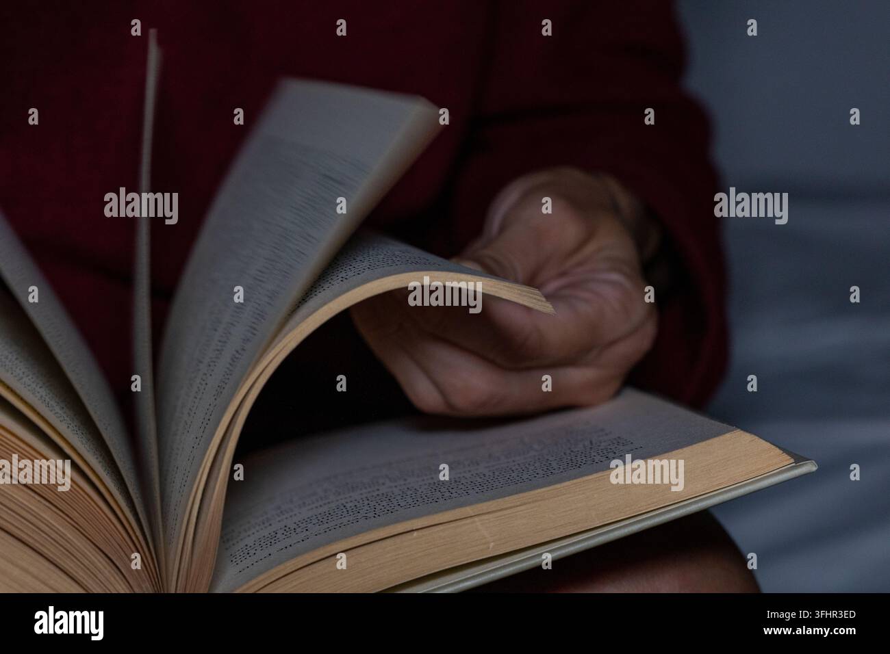 Scatto dettagliato di mani che sfogliano le pagine di un libro aperto in un ambiente buio. Foto Stock