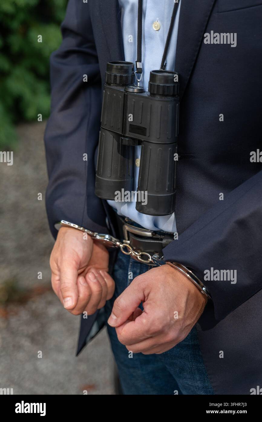 Binocolo e manette simboleggiano la raccolta illegale di informazioni, la sorveglianza segreta e la responsabilità legale per violazioni della privacy Foto Stock