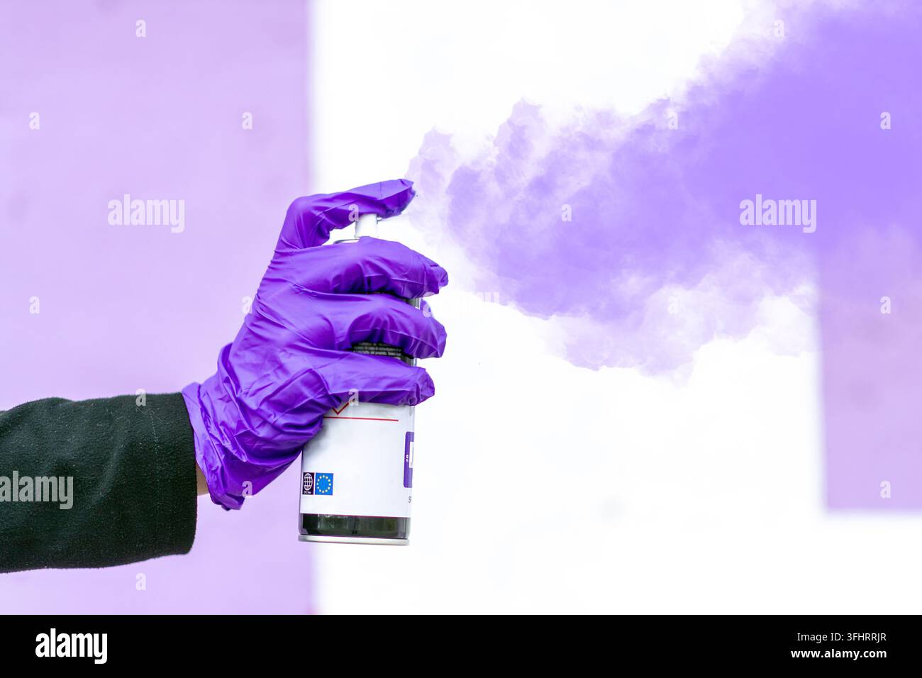 Mano guantata di viola che spruzza nebbia di vernice Foto Stock