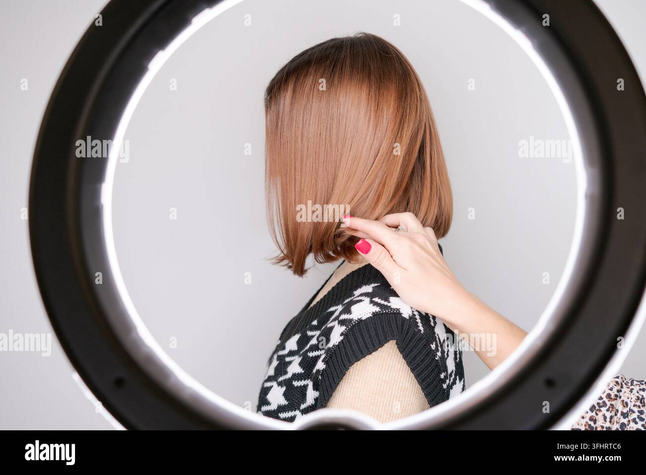 Donna con capelli tinti in una lampada ad anello circolare, il maestro raddrizza la cliente Foto Stock