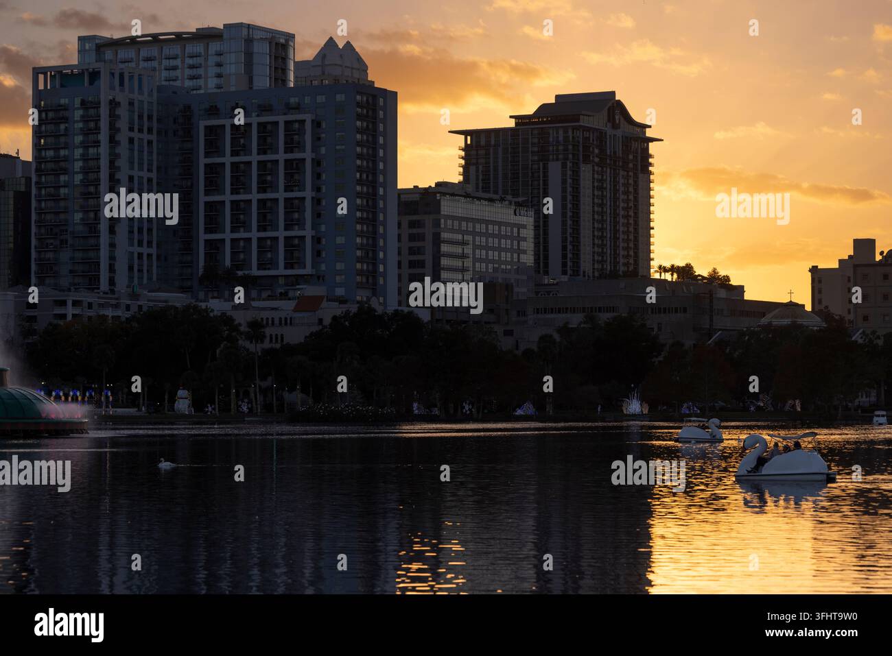 Orlando, Florida, USA – 23 dicembre 2025: Persone remano in barche a forma di cigno davanti allo skyline del Lake Eola nel centro città. Foto Stock