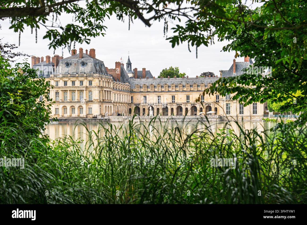 Vista scenografica dello Chateau de Fontainebleau in Francia, una residenza reale storica intravista attraverso una vegetazione lussureggiante sul lungolago. L'architettura elegante e la serenità. Foto Stock
