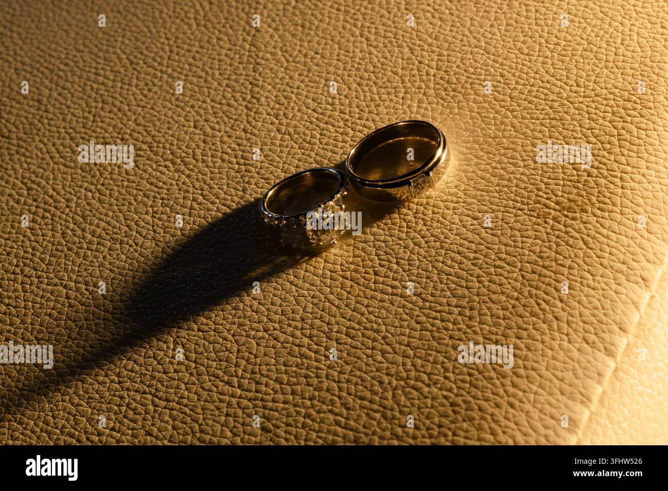 Eleganti anelli di matrimonio con diamanti su superficie in pelle strutturata con illuminazione calda Foto Stock
