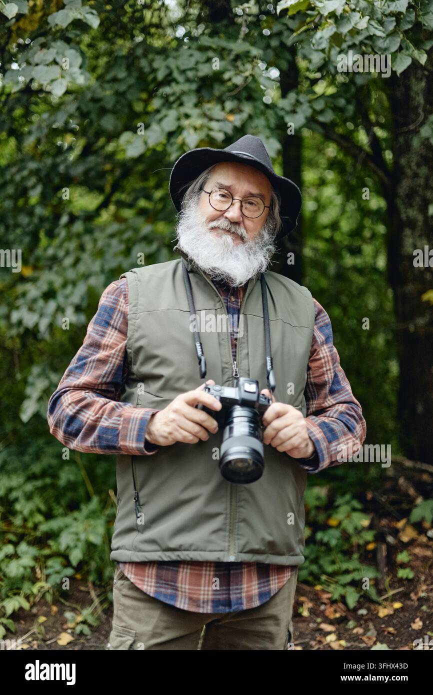 Ritratto di un uomo anziano che tiene una fotocamera digitale nella foresta Foto Stock