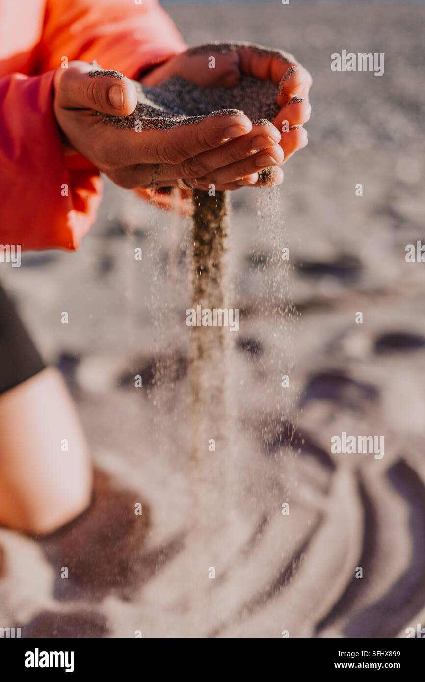 Mani con sabbia che scorre dalle dita su una spiaggia soleggiata che rappresentano il concetto del tempo che passa e dell'eternità Foto Stock