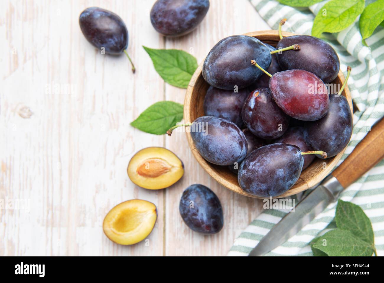 Prugne fresche in una ciotola di legno con coltello Foto Stock