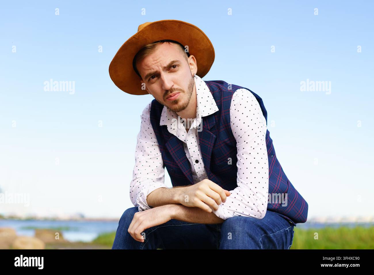 Ritratto di un giovane uomo adulto con cappello, camicia bianca e gilet sullo sfondo della natura Foto Stock