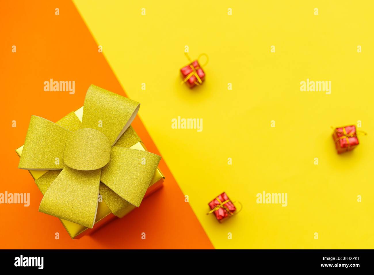 Scatola regalo giallo brillante con fiocco e nastro dorati su giallo e arancione Foto Stock