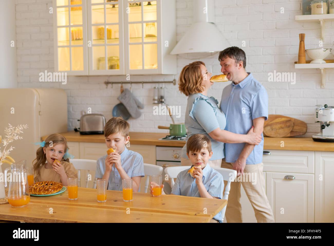 Una famiglia allegra in cucina, bambini che giocano a tavola e genitori che ballano Foto Stock