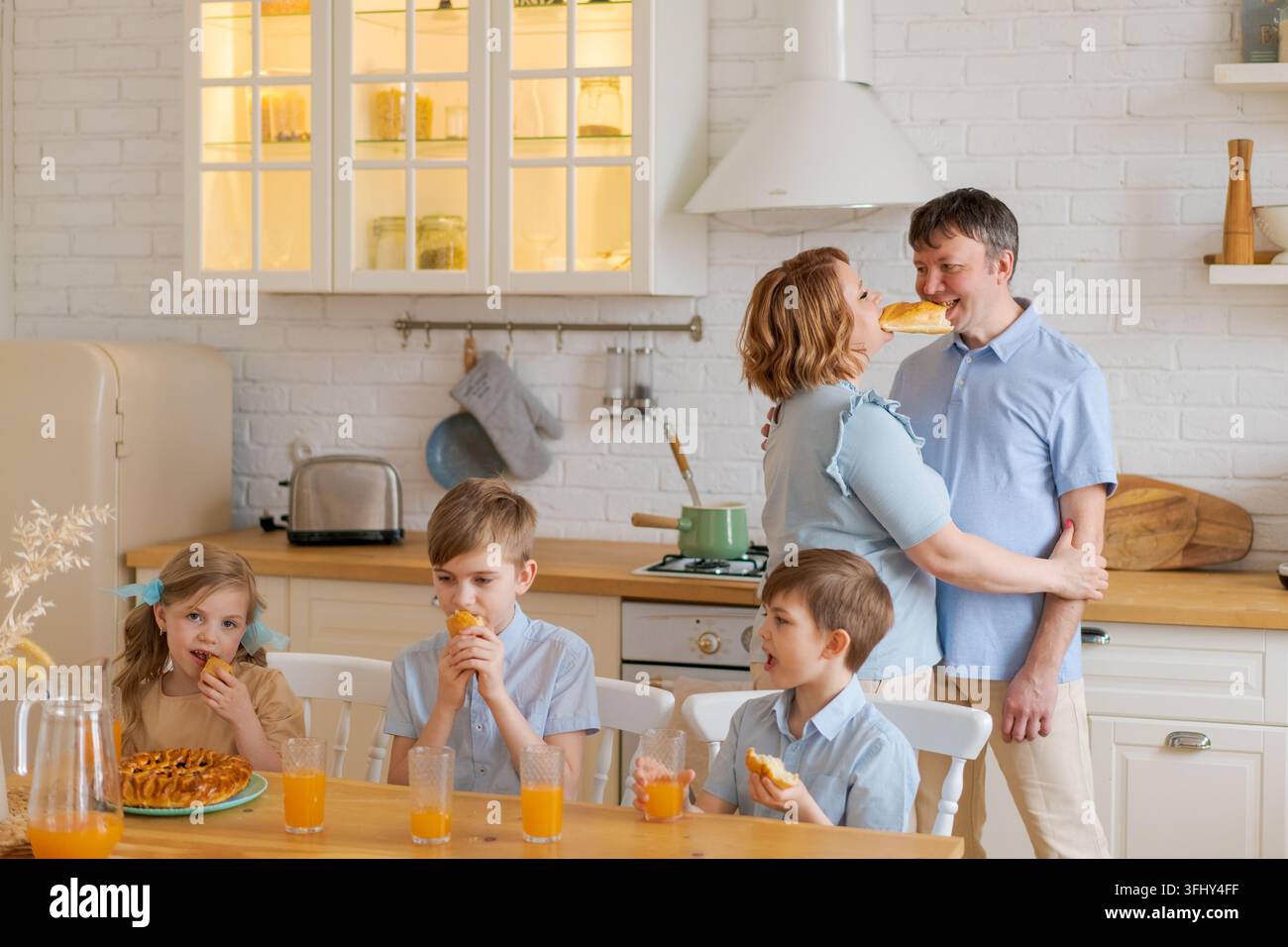 Una famiglia allegra in cucina, bambini che giocano a tavola e genitori che ballano Foto Stock
