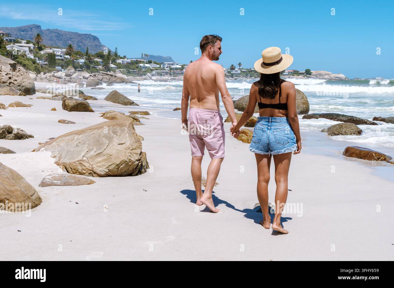 Coppia che cammina mano nella mano lungo le spiagge sabbiose di Camps Bay, Città del Capo, Sudafrica Foto Stock