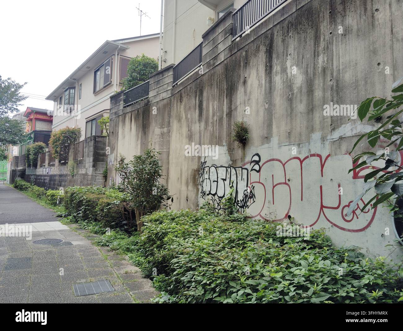 Tag di graffiti su un muro di sostegno in cemento lungo una stretta strada residenziale a Tokyo, Giappone. Foto Stock