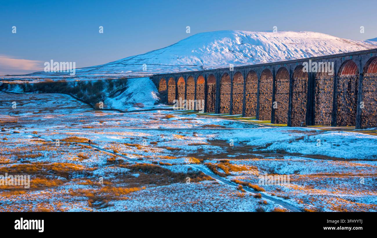 La luce dorata del sole illumina il viadotto di Ribblehead e la montagna innevata di Ingleborough nelle Yorkshire Dales, North Yorkshire, Inghilterra. Foto Stock