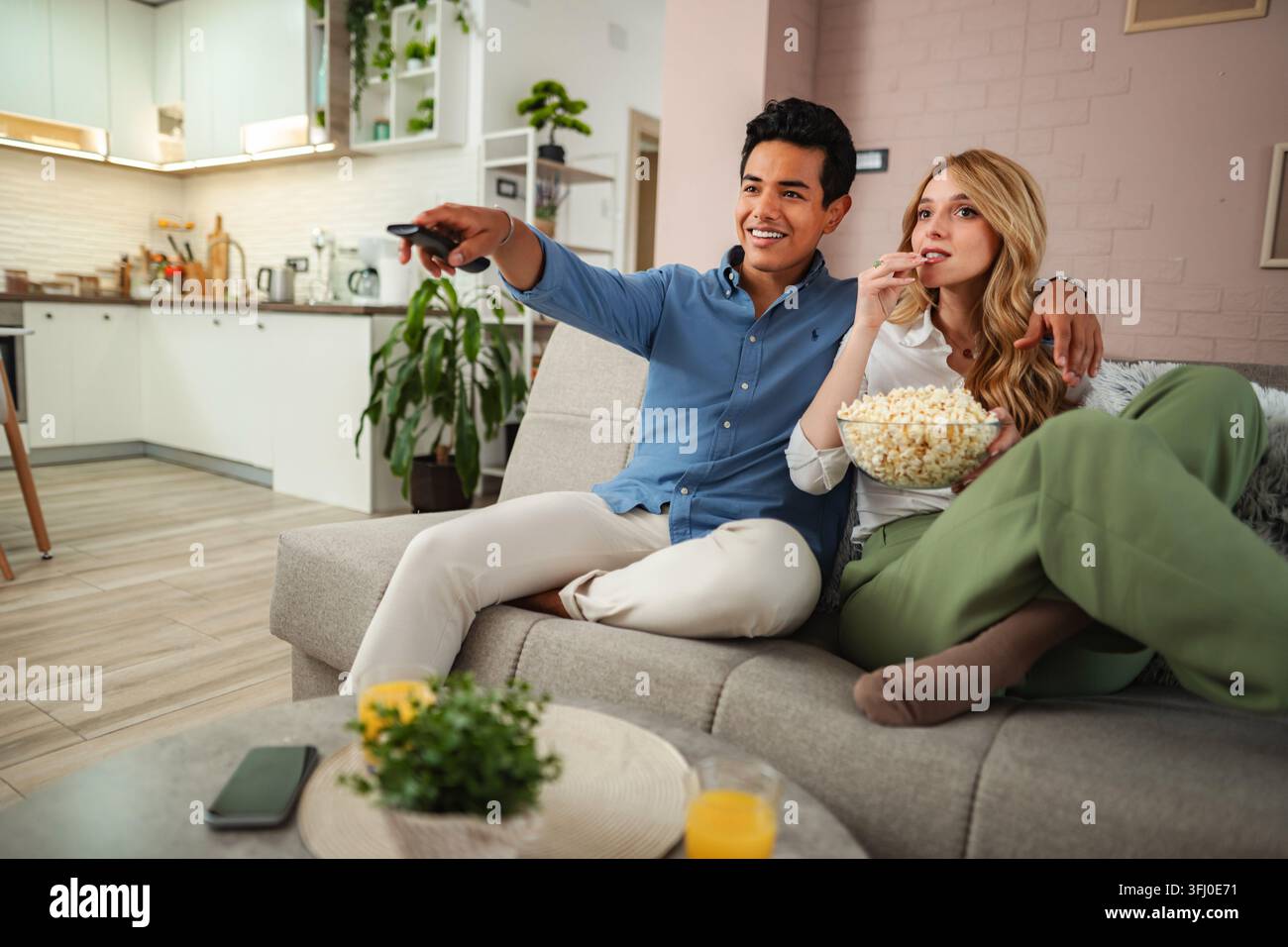 Coppia che si rilassa sul divano guardando la TV mangiando popcorn Foto Stock